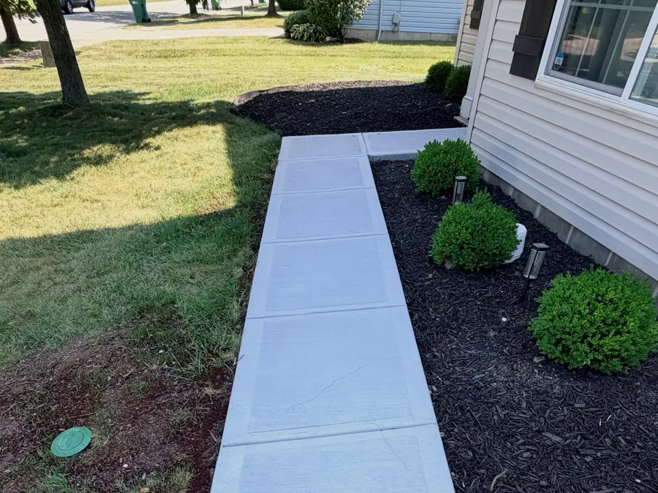 Straight concrete walkway along a house and mulched planting bed